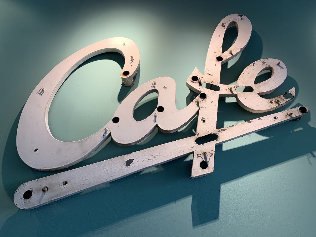 Der abgenommene Leuchtschriftzug Cafe lehnt an einer petrolgrünen Wand
